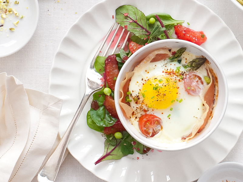 Baked eggs in ramekin dish with green salad on a plate